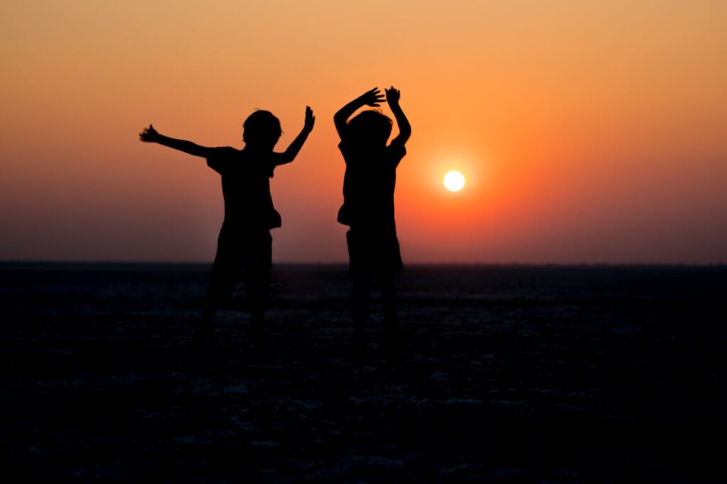Two children joyfully silhouetted against a vibrant sunset, creating a picturesque scene.