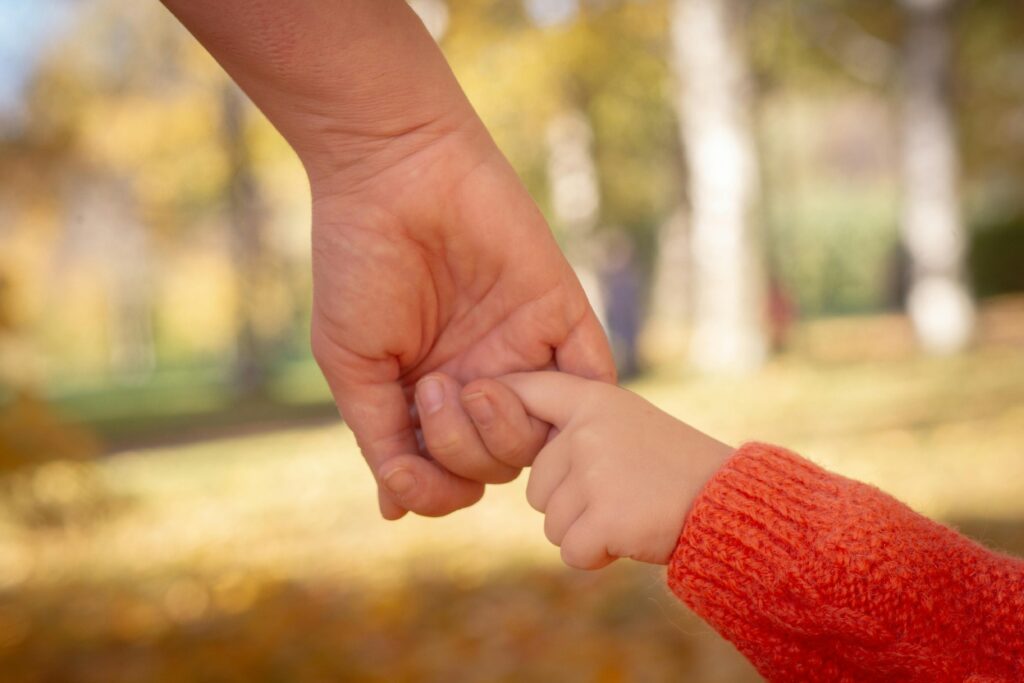 Close-up of a child's hand in an adult's hand, conveying care and trust in a park setting.